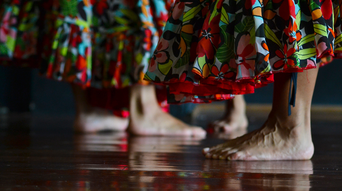 A close up of two dancers bare feet and their red flower-patterned skirts.